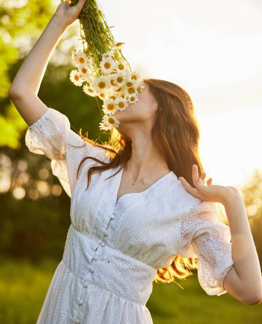 vertical portrait of a red-haired woman in nature during sunset sniffing a bouquet of daisies. High quality photo